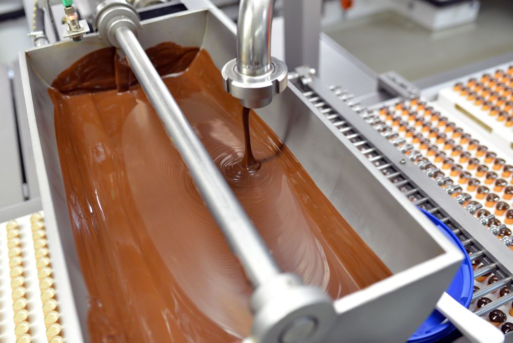 flüssige Schokolade in einer Fabrik zur Herstellung von Pralinen und Süßwaren in der Industrie // liquid chocolate at a factory